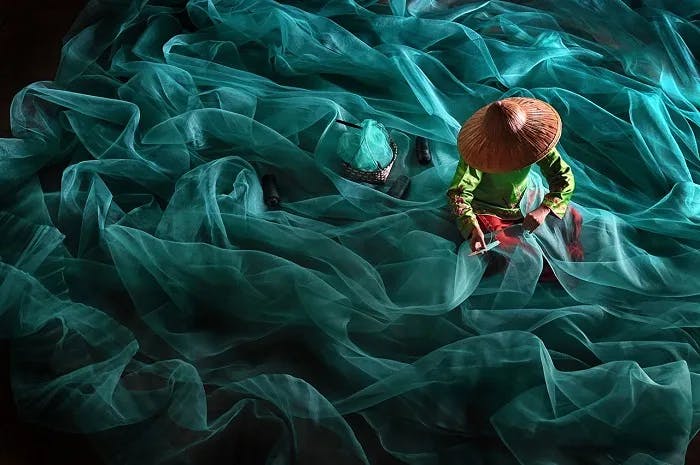 A woman is weaving a fishing net that curves like ocean waves
